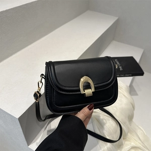 Klassische schwarze Satteltasche aus Leder mit goldener Hufeisenschnalle auf weißem Sockel