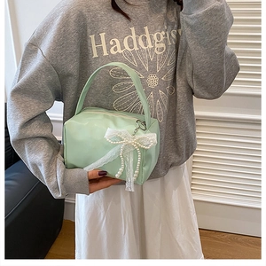 Detail of mint green leather makeup bag featuring a white lace bow and pearl charm