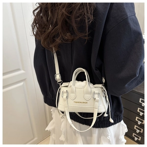 Close-up of white mini shell bag featuring gold fashion lettering and adjustable strap