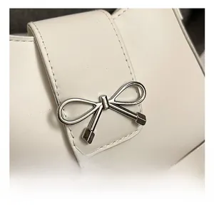 Macro detail of silver bow clasp and stitching on white leather underarm baguette bag