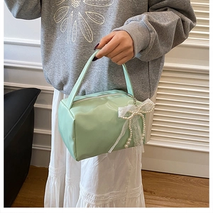 Detail of mint green square handbag featuring white lace bow and faux pearl chain charm