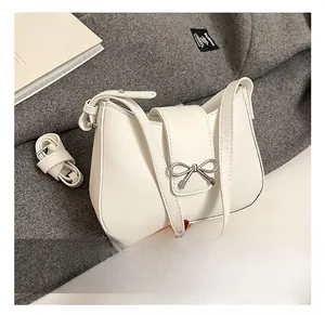 Close-up of a white leather baguette bag with a silver bow buckle and adjustable strap