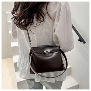 Close-up of a glossy dark brown underarm bag with a vintage buckle on white stairs