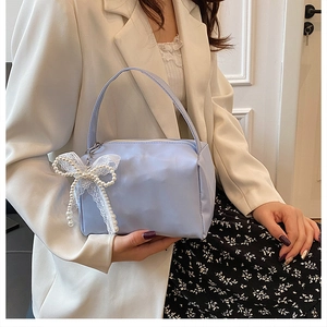 Detail of light blue mini square bag featuring a pearl and lace bow charm with zip closure
