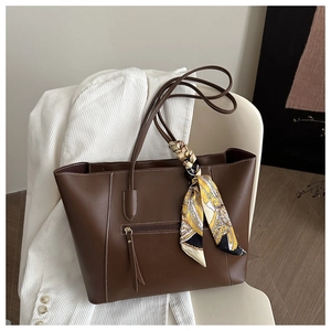 Detail of deep brown tote bag featuring smooth leather texture and decorative silk scarf