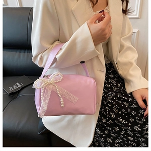 Pink cylindrical handbag with white lace bow and pearl charm detail held by a model