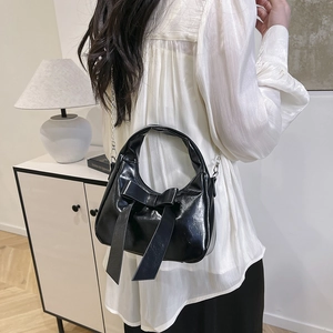 Glossy black patent leather bow handbag with silver chain strap shown in a modern interior
