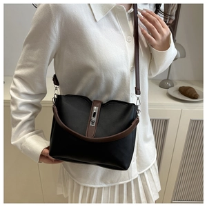 Detail of a minimalist black and brown bucket bag showing the silver metal clasp and PU leather