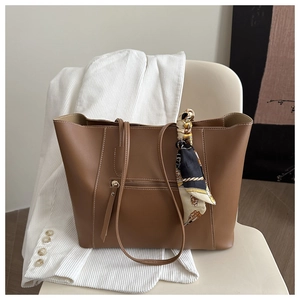 Close-up of caramel leather tote bag with a vintage floral scarf on a minimalist chair