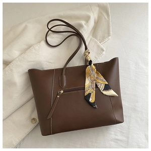 Detail of brown matte leather tote bag featuring a metal zipper pocket and silk scarf wrap