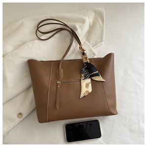 Detail of brown leather tote bag with white contrast stitching and decorative scarf