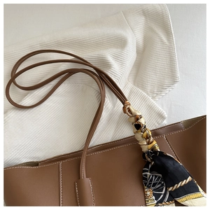 Detailed view of a brown leather tote bag with white stitching and floral scarf handle