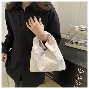 Detail of cream woven tote bag with knotted handle and premium leather texture