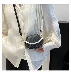 Détail d'un sac coquille noir avec anse en perles élégante et boucle métallique dorée chic