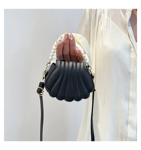 Détail d'un sac à main noir en forme de coquillage avec poignée en perles sur modèle