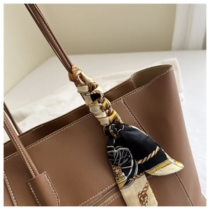 Detail of a brown tote bag featuring white contrast stitching and a silk scarf on the handle