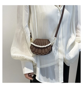 Detail of dark brown shell-shaped bag with pearl accents and golden metal hardware