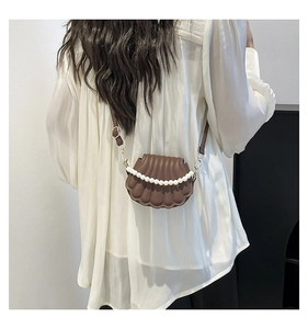 Brown shell-shaped crossbody bag with pearl chain detail shown on a model's shoulder