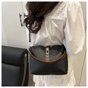 Minimalist black leather bucket bag with brown strap shown on model in a modern room