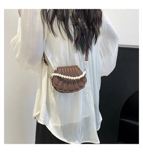Detail of a dark brown shell-shaped crossbody bag with pearl handle and leather strap