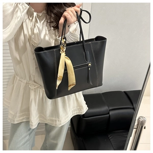 Detail of black leather tote bag featuring white contrast stitching and silk scarf accessory