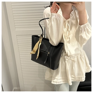 Detail of black tote bag with yellow silk scarf handle and front zipper on casual outfit