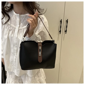 Detail of black bucket bag featuring brown leather trim and rectangular silver metal lock