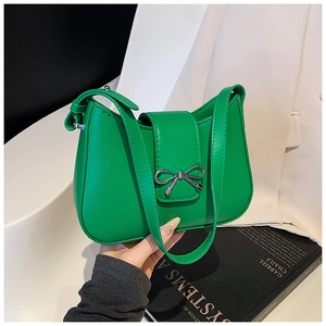 Détail du sac selle vert brillant avec un nœud en métal argenté et une bandoulière cuir