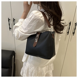 Detail of black leather bucket bag with brown handles and silver rotating lock