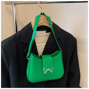 Détail du sac sous l'aisselle vert vif avec boucle noeud argenté sur fond de costume noir
