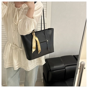 Detail of black leather tote bag with white stitching and decorative silk scarf handle