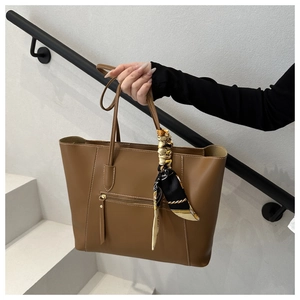 Detail of a brown leather tote bag with side zipper pocket and decorative silk scarf