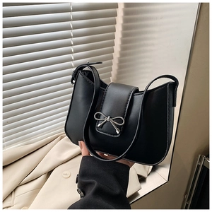 Détail d'un sac sous le bras en cuir noir avec boucle de nœud argenté sur un blazer beige