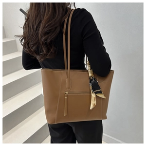 Detail of a brown leather tote bag with silk scarf on handle and front zipper pocket