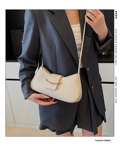 Detail of a creamy white crescent bag with a gold metal clasp and smooth leather texture