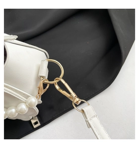 Detailed macro view of white shell bag with gold lobster clasp and luxury pearl strap