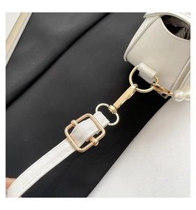 Detail of white leather shell bag with gold hardware and elegant pearl handle strap