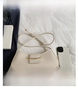 Detail of a beige half-moon shoulder bag with gold buckle next to a smartphone