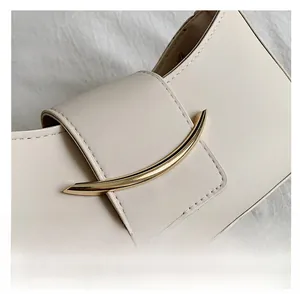 Detail of minimalist beige leather underarm bag featuring a gold crescent metal buckle
