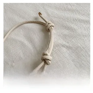 Detail of cream leather shoulder bag with round cord handle and gold metallic caps