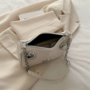White croissant shoulder bag with silver grommets and chain strap in a chic setting