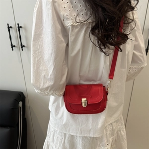 Red pebbled leather saddle bag with gold metal buckle shown on a model in a modern home