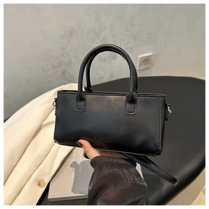 Modern black leather handbag with fashion lettering held against a minimalist background