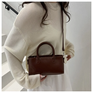Brown leather handbag with double handles and fashion embossing worn by a model