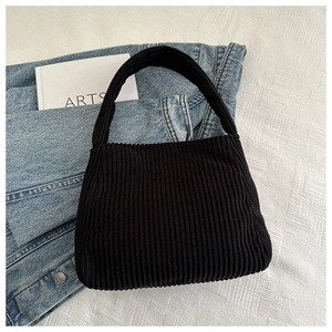 Detail of black corduroy shoulder bag showing ribbed texture on a denim jacket background