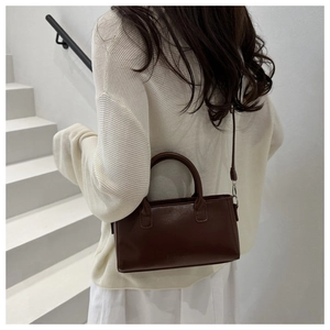 Detail of minimalist dark brown rectangular crossbody bag worn with casual white outfit