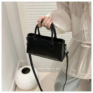Close-up of a black minimalist rectangular handbag with sleek round handles and strap