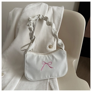 Close-up of white fabric underarm bag featuring pink embroidered bow and ruffled handle