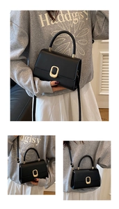 Detail of black faux leather handbag showing golden oval buckle and adjustable shoulder strap