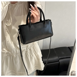 Detail of a black square leather handbag featuring embossed fashion lettering and a slim strap